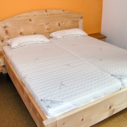 Doppelbett Kranzhorn mit extra aufgesetztem Segmentbogen auf dem gerahmten Kopfhaupt, freischwebend angesetzten Nachttischen und Fußbereich auf zurückgesetzten Unterbausockel - Original Steiner Zirbenbett