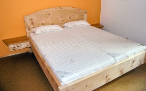 Doppelbett Kranzhorn mit extra aufgesetztem Segmentbogen auf dem gerahmten Kopfhaupt, freischwebend angesetzten Nachttischen und Fußbereich auf zurückgesetzten Unterbausockel - Original Steiner Zirbenbett