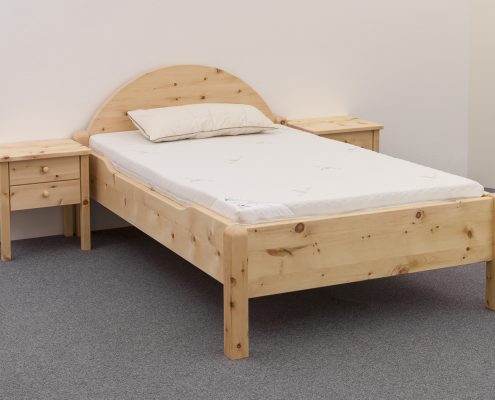 Einzelbett Sterneck, massive Alpenzirbe, Kopfhaupt mit markantem Segmentbogen, abgesenkte Seitenwange, Eckpfosten gerundet, Abb. mit optionalen Nachtkästchen und mit optionalem ergonomischer Komfortzone aus ProNatura-Schlafsystem - Original Steiner Zirbenbett