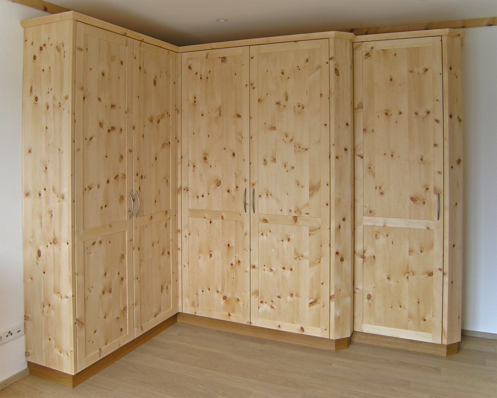 Zirbenholz-Kleiderschrank 09.6, Eckschrank aus massiver Zirbe, abgeschrägte Korpuskanten, gerades Aufsatzgesims, Eichen-Sockel, 5 Rahmentüren mit abgeplatteten Füllungen, 1 Türelement zurückgesetzt, passend zu Original Steiner Zirbenbetten