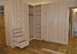 Zirbenholz-Kleiderschrank 09.4,. Eckschrank-Maßeinbau, 6 Türen, 4 Schubladen, zusätzliches Fach oberhalb der Zimmertür mit Türen, Messingknöpfe an Tür- und Schubladenfronten, massives Zirbenholz, Regalböden, Kleiderstange im Eckfach, Kleiderlift im rechten Schrankteil, passen zu Original Steiner Zirbenschlafzimmer