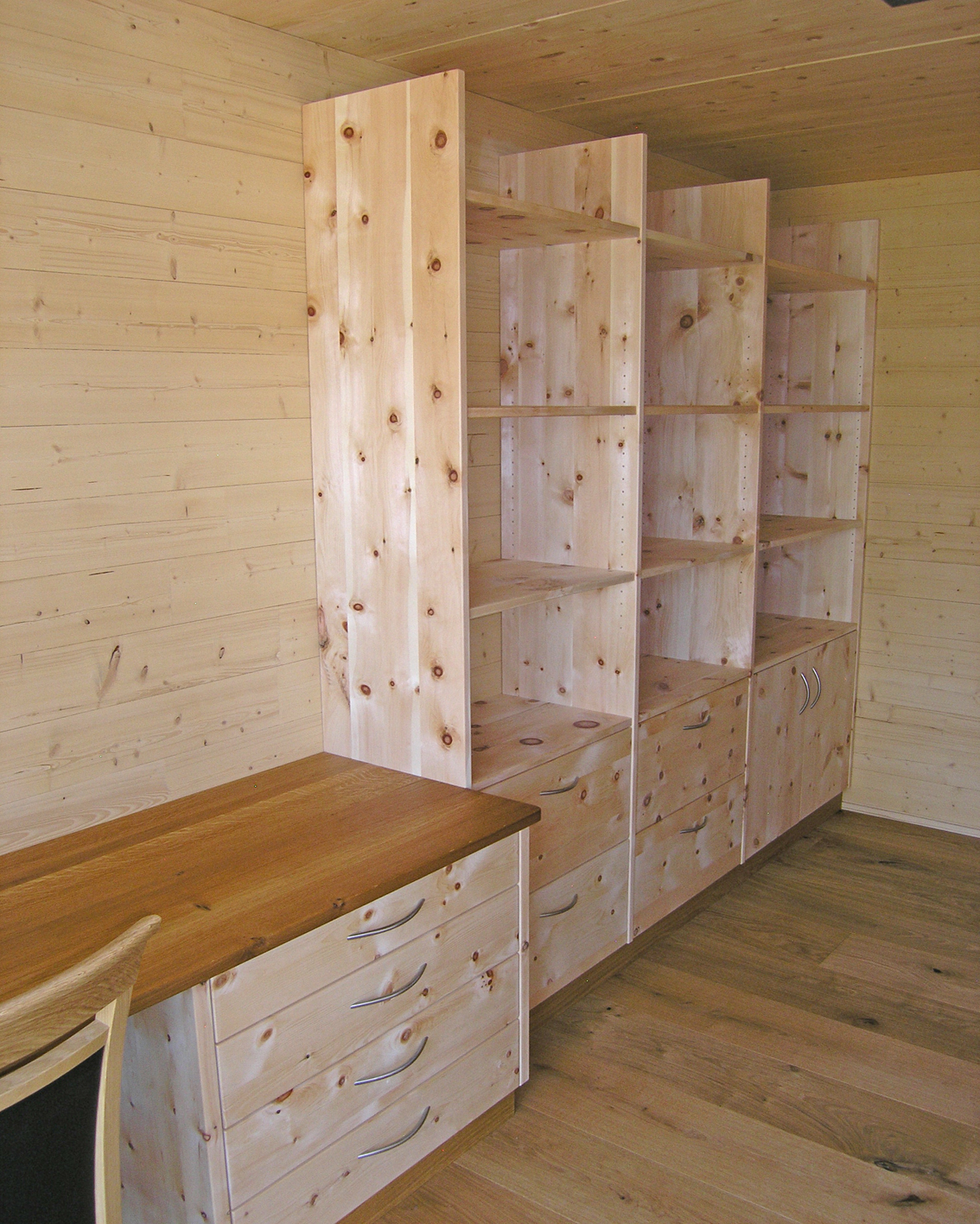 Zirbenholz-Regalwand 08.1, massive Zirbe, Unterteil als Kommode mit Schubladen und Türen, angebauter Schreibtisch, Deckplatte aus Eiche, passend für einen Arbeitsraum mit ruhiger Atmosphäre