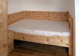 Einzelbett in Sondermaßen als Variante des Original Steiner Zirbenbett Traithen, hier speziell auf die örtlichen Gegebenheiten in eine Nische eingepasst, mit dreiseitigem Wandschutz, dazu passendes Nachtkästchen plus Schrank und in der Größe angepasstem ProNatura-Schlafsystem